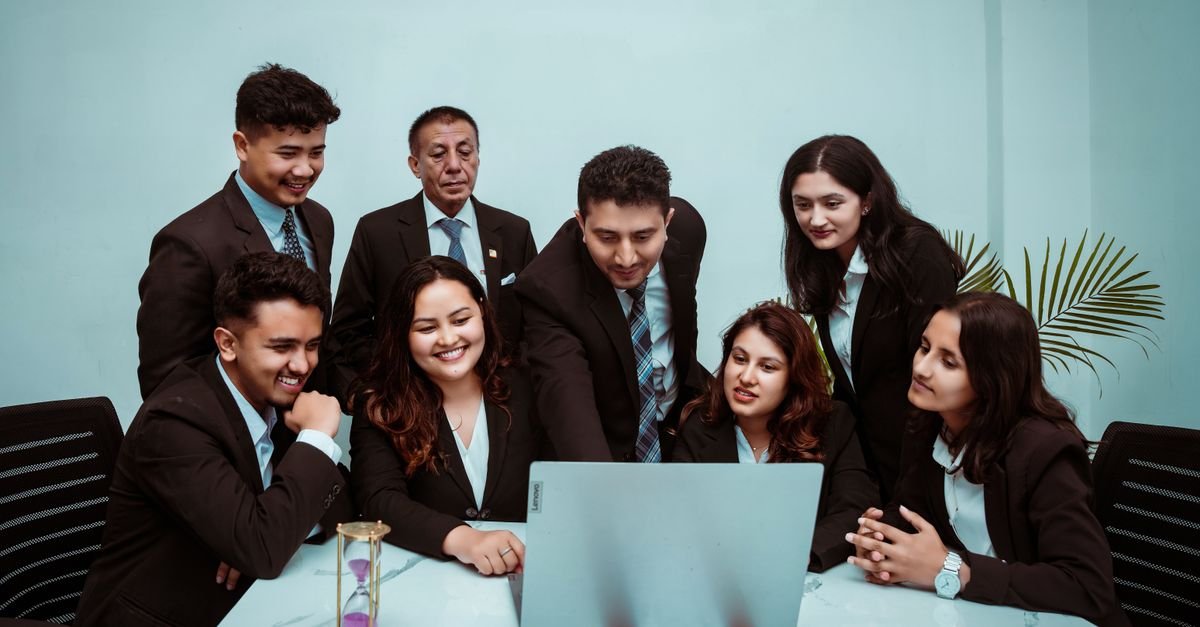 A diverse team of professionals collaborating around a laptop in a modern office setting.